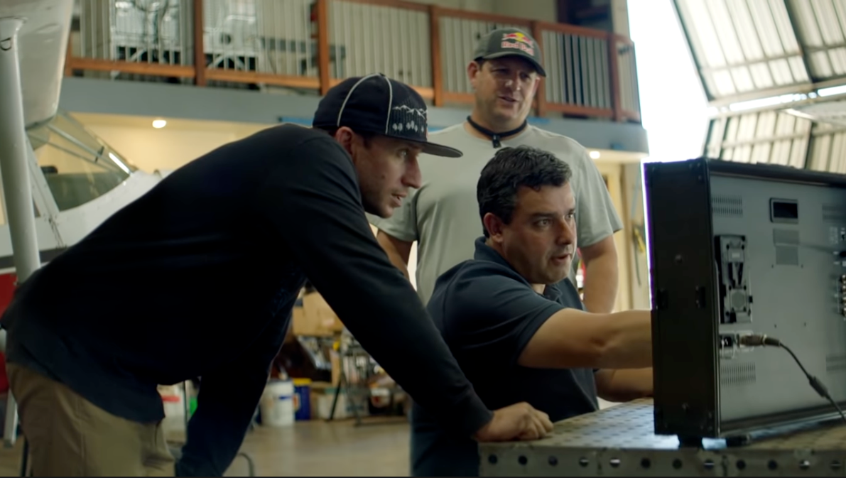 Red Bull Plane Swap pilots Andy Farrington (at left) and Luke Aikins (far right) study the aerodynamics of the planes' speed brakes with aerodynamicist Dr. Paulo Iscold. - Red Bull Plane Swap Debacle