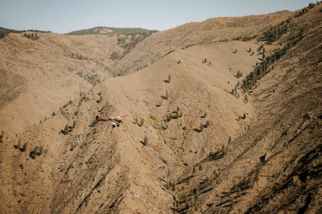 Dykstra, piloting an A-1C Aviat Husky, stands out among Idaho's dry terrain. Smoke and wildfires are common in warmer months. [Credit: Jordan Lefler]