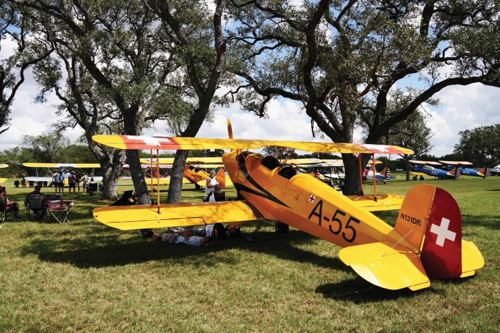 Pilots rest under the shade of a Bucker Jungmann during the heat of the day at the Under the Wire Fly-In. [Credit: Cayla McLeod]